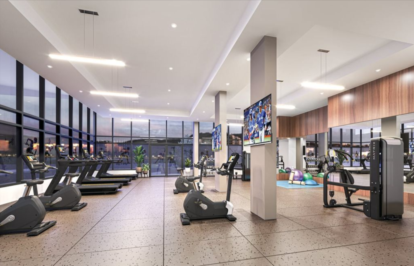 Modern gym with large windows, treadmills, stationary bikes, weight machines, exercise balls, and TV screens, well-lit by ceiling lights.
