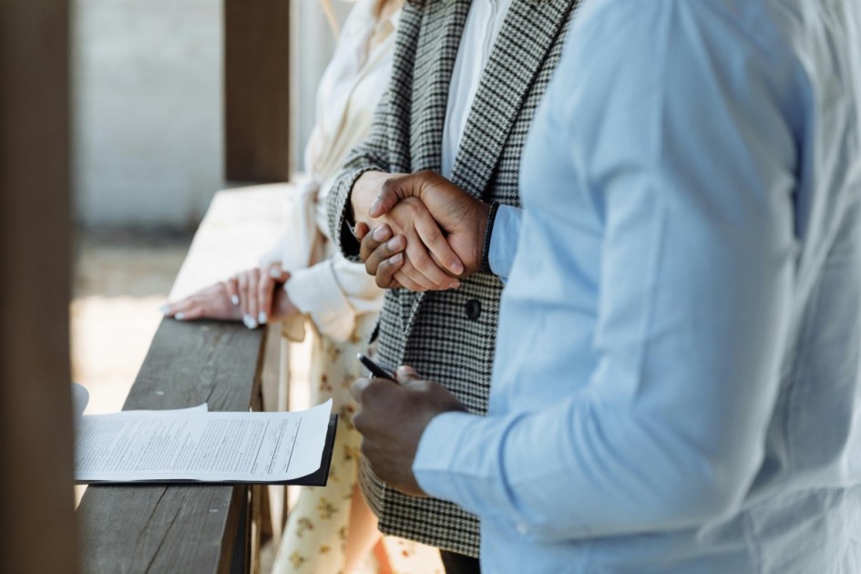 two hands shake near a clipboard with a home closing contract